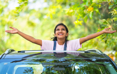 Enjoying girl feeling fresh air nature by stretching arms on car sunroof - concept of freedom, refreshment and summer holidays