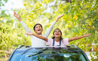 Happy young sibling feeling fresh air by shouting on car sunroof - concept of childhood lifestyle,...