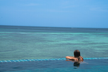 Woman in the infinity pool of a hotel while watching the sea