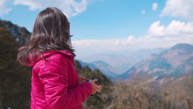 Young Indian woman photographer holding camera in hand and looking at the nature mountains view at Jalori Pass, Himachal Pradesh, India. Travel photographer on location for shoot.