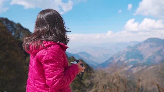 Young Indian female tourist observing shots in camera after shooting while standing outdoors at Jalori pass, Himachal Pradesh, India. Travel and holiday concept.