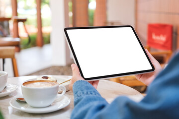 Mockup image of a woman holding digital tablet with blank white desktop screen with cake and coffee cup on the table in cafe