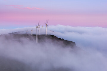 Wind turbines on hill top in morning fog at sunrise