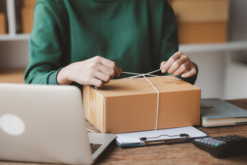 An woman tying a parcel to a customer's box, she owns an online store, she packs and ships through a private transport company. Online selling and online shopping concepts.