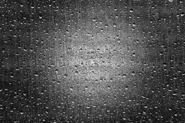 Water droplets on opaque glass window in black and white with a headlight shining through