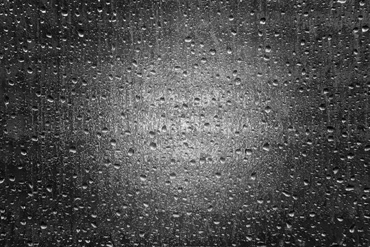 Water droplets on opaque glass window in black and white with a headlight shining through