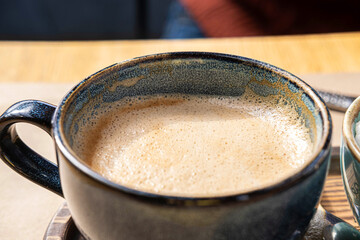 Blue Ceramic Cup of Hot Cappuccino with Foam on Wooden Cafe Table. Beautiful Latte with bubble Froth. Trendy Authentic Modern Porcelain Set. Pottery Handmade Coffee Mug Served with a Sugar Bowl