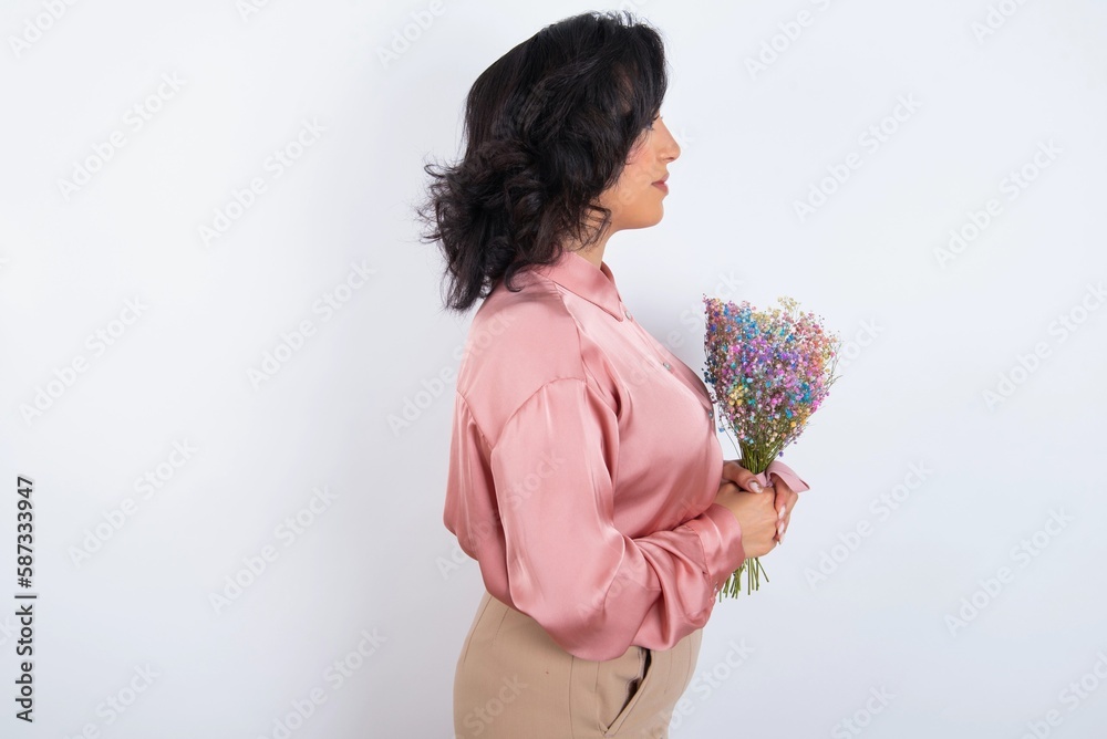 Wall mural young woman holds big bouquet of nice flowers over white background looking to side, relax profile pose with natural face with confident smile.