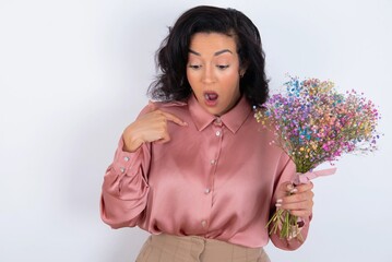 Shocked young woman holds big bouquet of nice flowers over white background look surprisedly down,...