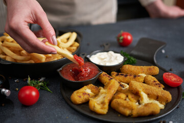 Woman dips french fries into dip sauce with Cheese fried mozzarella sticks on a table