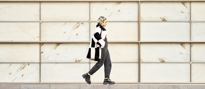 Stylish woman walking on street near fence