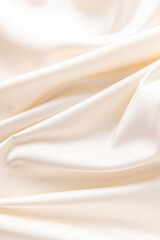 luxurious wedding satin background with delicate folds. elegant satin fabric of beige color, ivory. vertical view.