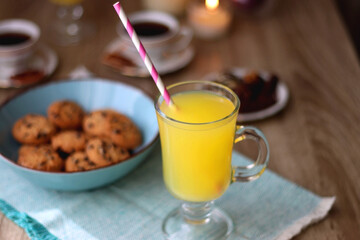Plate of chocolate pralines, bowl of cookies, cups of tea, glasses of juice and lit candles on the table. Selective focus.