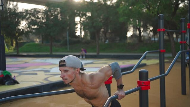 Muscular man doing push ups exercises on parallel bars. Male athlete workout outdoor gym, Strength and motivation. Medium shoot front view. Bodyweight training. Naked torso