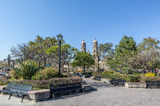 Plaza de las Americas with green trees and pedestrian paths against blue sky, Basilica of Our Lady of Zapopan in background, sign: keep off the grass, Mexican cityscape on a sunny day, Jalisco, Mexico