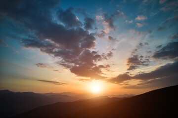 Panoramic view of bright evening sun and dramatic cloudy sky over mountains. Magnificent scenery of mountain hills under colorful evening sky with clouds and setting sun. Beauty of nature concept.