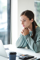 Vertical image of young confident businesswoman sitting at the office table focused working on laptop computer