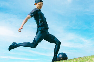 青空の下でサッカーボールを蹴る日本人男性 - obrazy, fototapety, plakaty