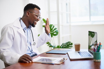 Happy friendly doctor waves hello to patient on telehealth call, remote visit