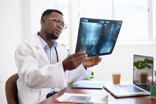 Serious looking Black doctor holds x-ray to diagnose patient in office