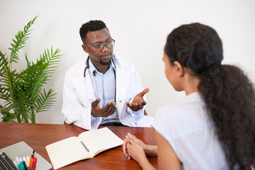 Black male doctor explains diagnosis to young female patient at GP visit