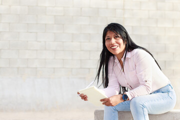 Mujer latina morena madura en jeans y blusa listada, con cabellos negro suelto sentada y mirando al...