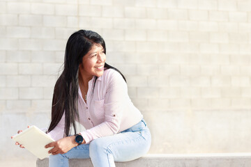 Mujer latina morena madura en jeans y blusa listada, con cabellos negro suelto sentada y mirando...