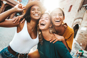 Three multiracial young women having fun walking on city street - Happy girlfriends hanging outside...