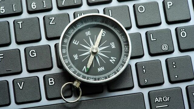 One single compass laying on a modern computer desktop PC keyboard, world navigation, different directions, NSWE object closeup, nobody, central composition, technology. Choosing a route, path concept