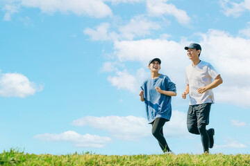 青空の下でジョギングをする笑顔の日本人男女 - obrazy, fototapety, plakaty