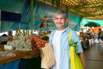 portrait senior man holding a yellow eco-friendly cloth bags to put vegetables and paper bag,...