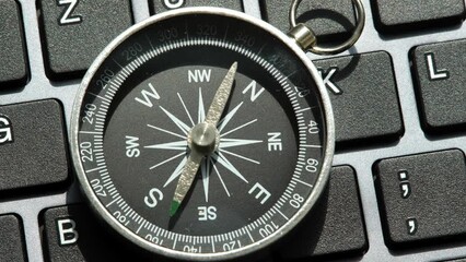 One single compass laying on a modern computer desktop PC keyboard, world navigation, different directions, object closeup, nobody, pan, technology. Choosing a route, tech career path concept - Powered by Adobe