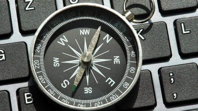 One single compass laying on a modern computer desktop PC keyboard, world navigation, different directions, object closeup, nobody, pan, technology. Choosing a route, tech career path concept