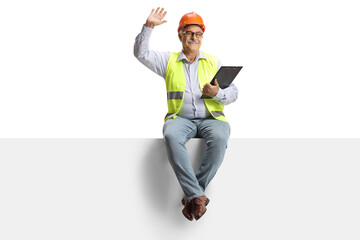 Full length portrait of a mature male engineer sitting on a blank panel and waving at camera