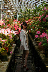 A brunette in a beige dress and glasses among blooming azaleas