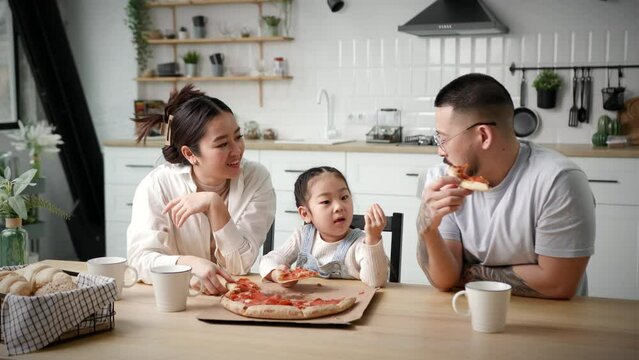 Happy Family Eating Pizza. Asian family with child eats pizza sitting at home. Parents chatting with kid during meal time.