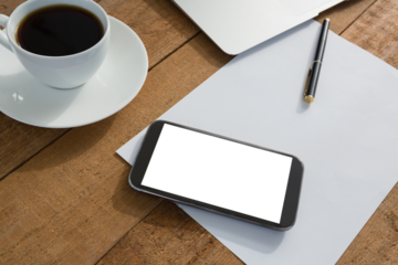 Laptop, mobile phone, black coffee, pen and paper on wooden plank