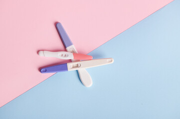 Flat lay composition with pregnancy tests stacked on blue and pink pastel background with copy ad space. Women's health, fertility and rapid pregnancy diagnostics concept