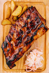 Pork loin ribs served on chopping board and potato wedges