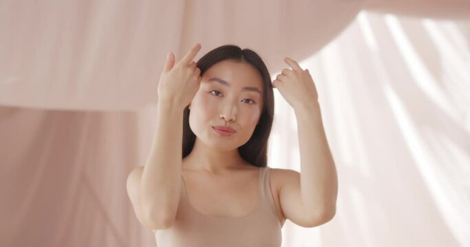 Asian woman touching clean face and admiring healthy, soft skin. Pretty model having happy, smiling and posing to camera. Showing natural beauty face. Beautiful view, good looking.
