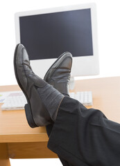 Cropped legs of man on desk by computer and keyboard 