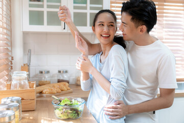 Happy Asian family cooking in kitchen at home, Husband surprises wife with gift on wedding...