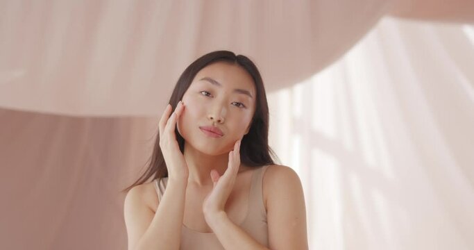 Close up of Asian happy girl with fresh nice skin. Young female posing to camera and showing beautiful face after cosmetic procedure. Face looking shining, soft and healthy. Cosmetology, makeup.