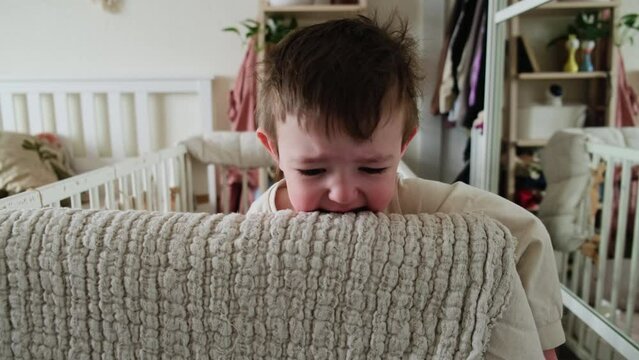 Toddler baby is naughty while standing in the crib. Sleepy child cries without tears, face close-up. Kid age one year nine months