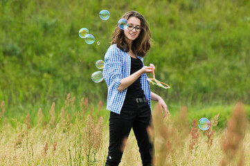 Young girl blowing soap bubbles in the meadow.