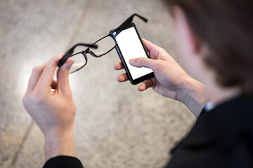 Man using smart phone while holding eyeglasses
