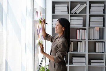 Successful smiling businesswoman writing note on post-it at office.