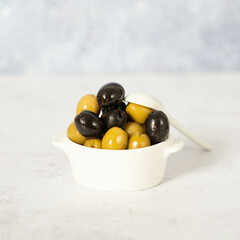 Delicious black, green and red olives with leaves in a wooden bowl, isolated on white background