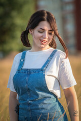 Portrait of a young beautiful dark-haired girl in a denim sundress on a summer field.