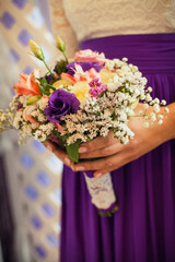 A girl in a white blouse and purple skirt holds in her hands a beautiful festive bouquet of flowers of yellow, purple, white, pink and red.